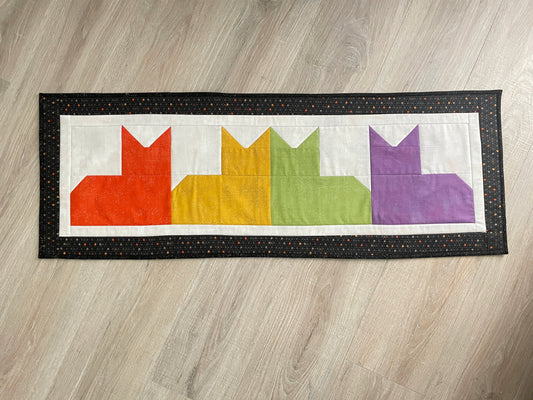 Quilted table runner with colorful patchwork cats and black border, reversible Halloween spooky eyes backing.