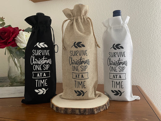 Burlap wine bags with “Survive Christmas One Sip at a Time” text in black or white, displayed with wine bottles.