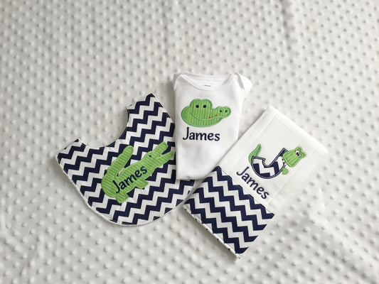 A personalized 3-piece alligator baby gift set including a white bodysuit, a navy chevron bib, and a matching monogram J burp cloth.