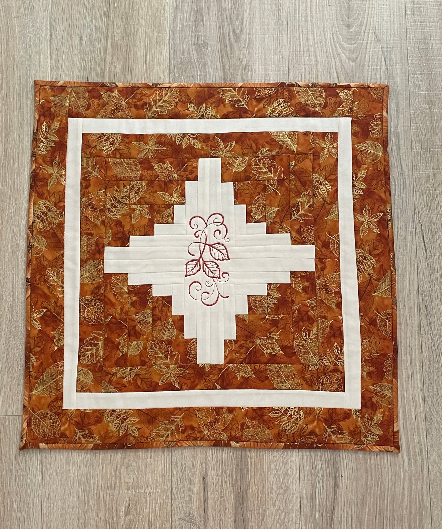 Fall table topper in rust and cream with embroidery in the center. The rust colored leaf fabric has hints of metallic threads.