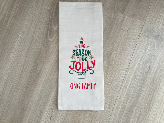 White cotton Christmas kitchen towel with personalized family name and festive holiday tree‑shaped text design.