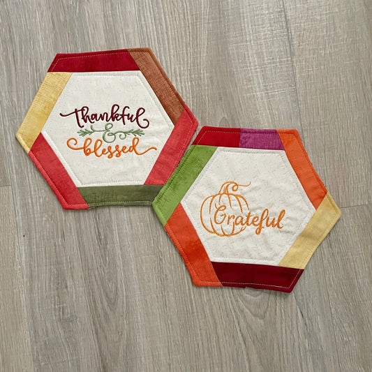 set of 2 handmade hexagon shaped mug rugs or fabric coasters with fall embroidery designs in the center panel.