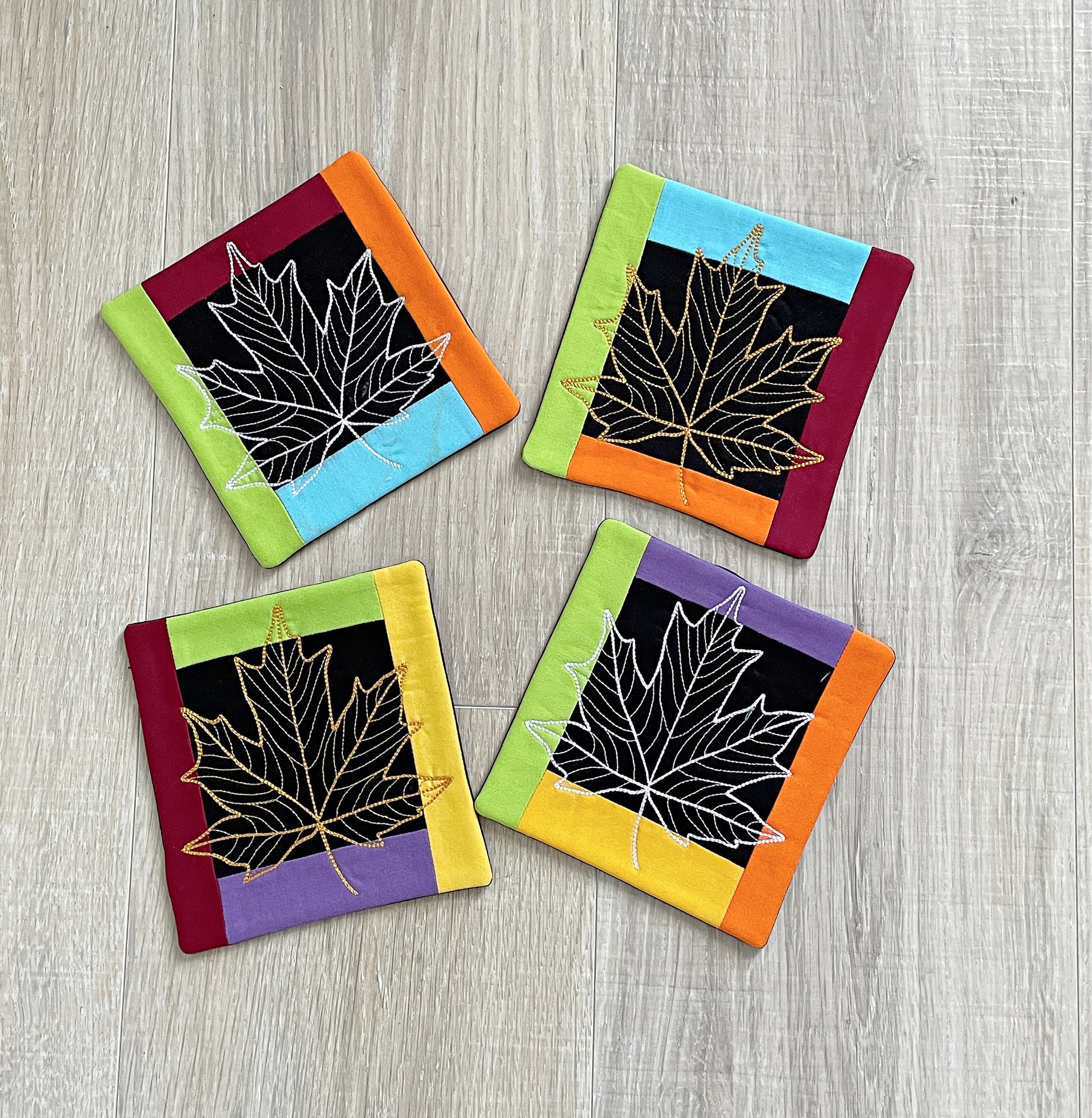 set of 4 fabric coasters for fall with machine embroidery of a maple leaf in the center of each coaster.