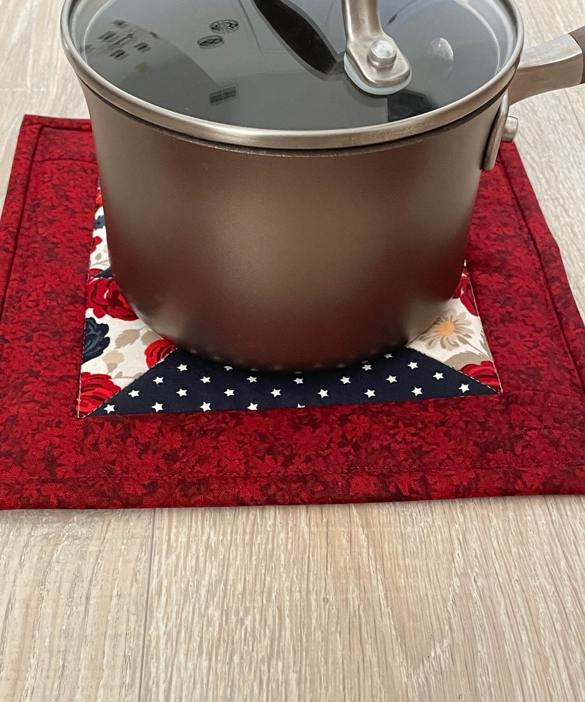 set of two quilted handmade potholders in country red cream and navy blue, flying geese pattern. Farmhouse or shabby chic decor. Beautiful florals and navy white star prints. Shown with cooking pot to show size.