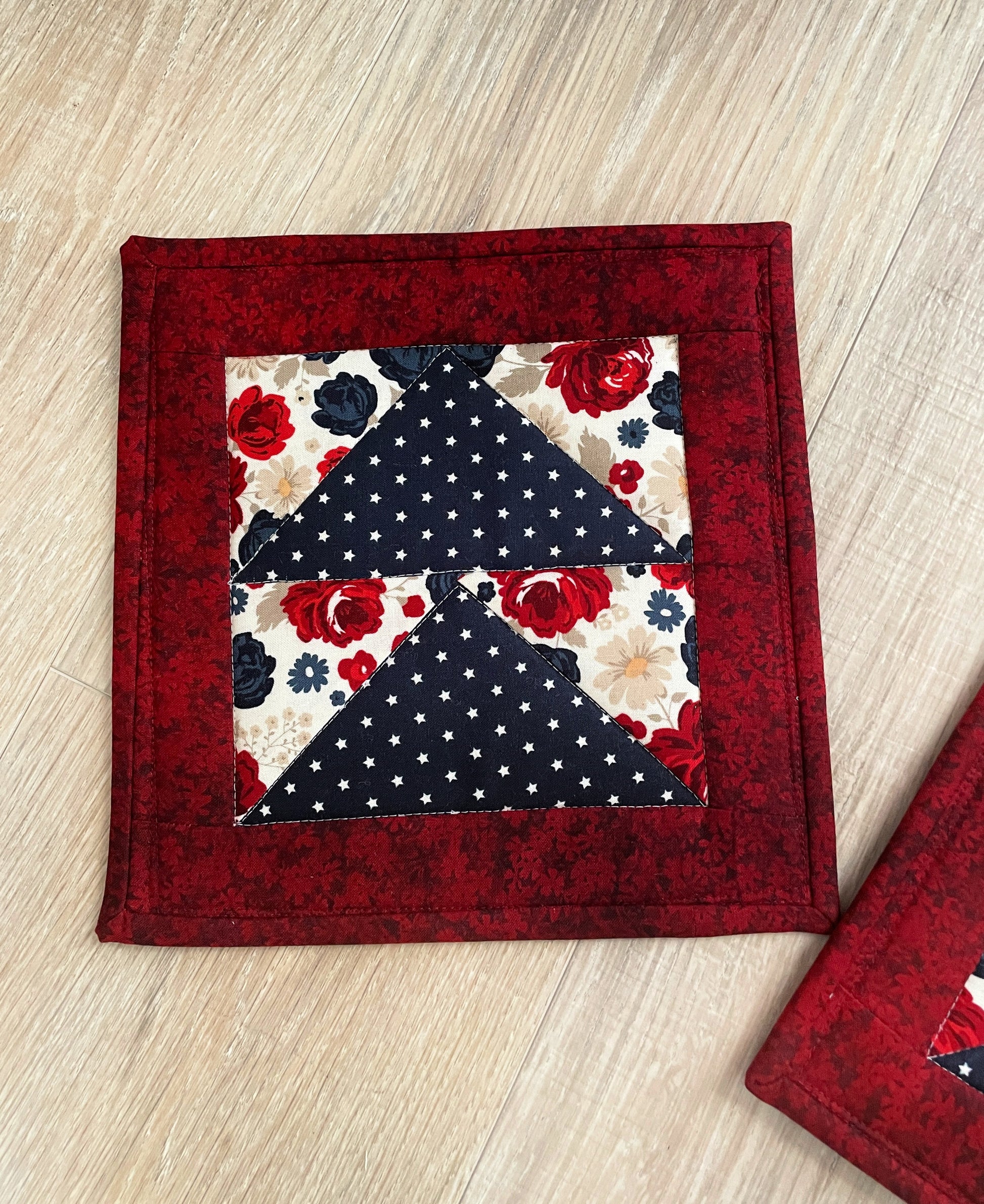 set of two quilted handmade potholders in country red cream and navy blue, flying geese pattern. Farmhouse or shabby chic decor. Beautiful florals and navy white star prints.