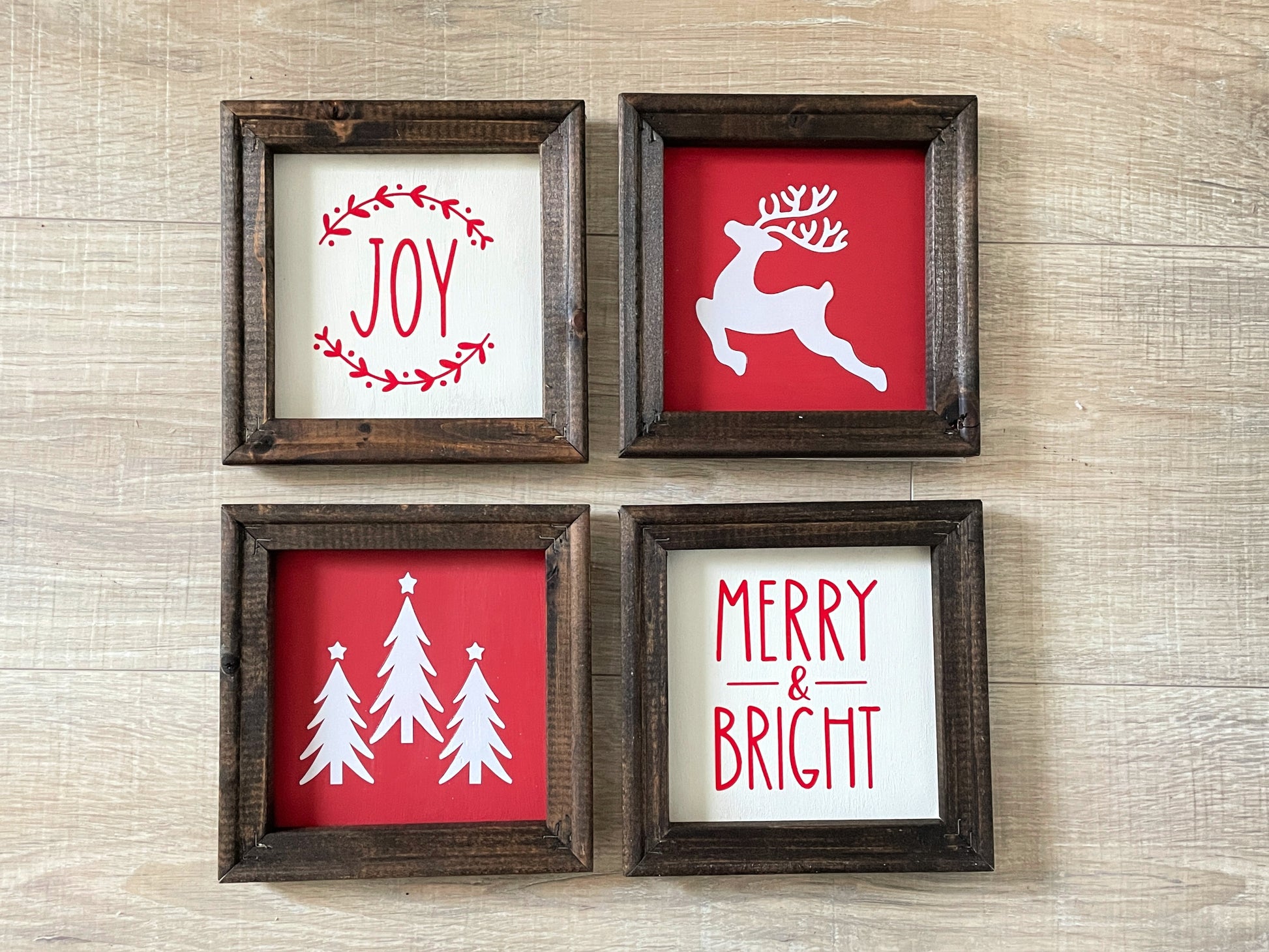 Set of four wood-framed Christmas signs featuring Joy wreath, reindeer, Christmas trees, and Merry & Bright designs in red and white farmhouse holiday colors.