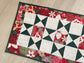 Handmade quilted Christmas table runner in red and green Hustle & Bustle fabric by Basic Grey, 13x26 inches.