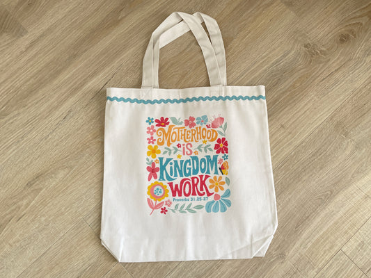 Handmade white cotton canvas tote bag featuring a colorful retro floral Motherhood is Kingdom Work Proverbs 31 print and a teal ric-rac ribbon trim.