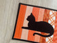 Quilted orange mug rug with black cat appliqué, handmade 8x10 snack mat.