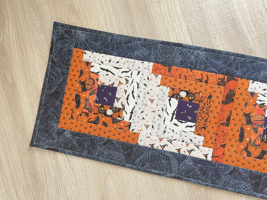 Scrappy Halloween quilted table runner with pumpkins, cats, and witchy prints