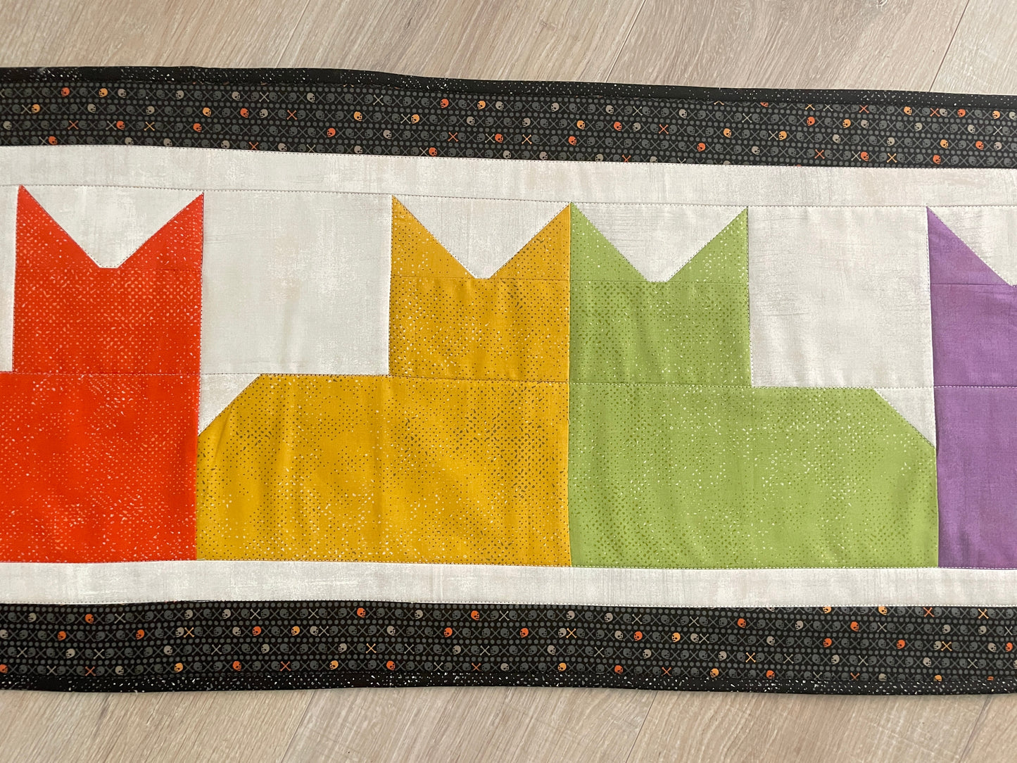 Quilted table runner with colorful patchwork cats and black border, reversible Halloween spooky eyes backing.