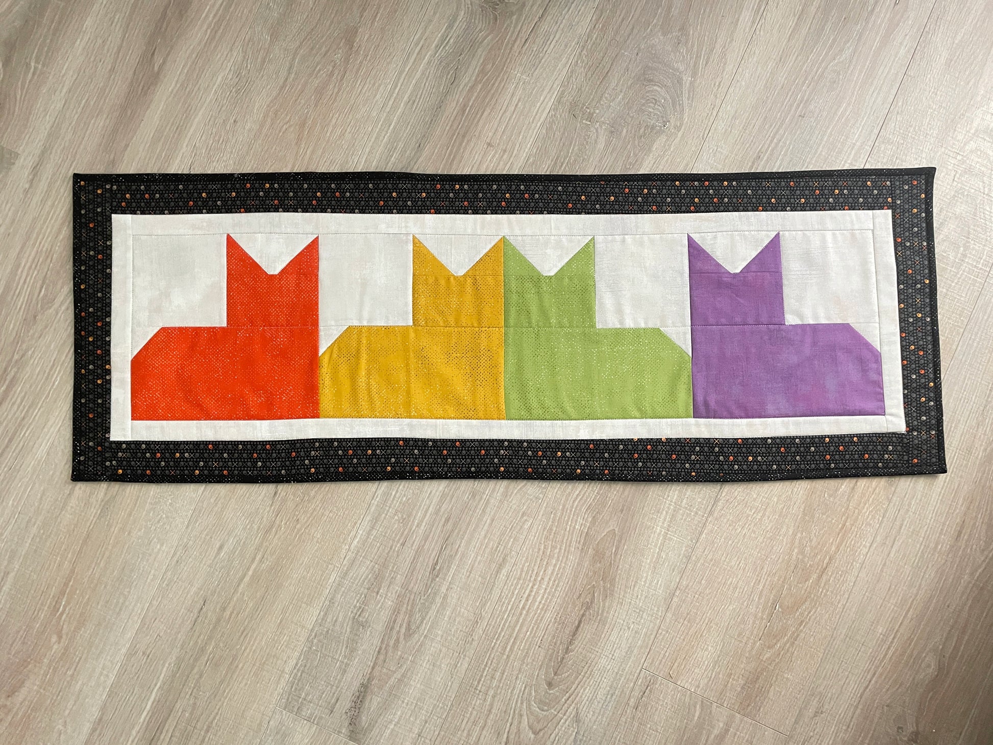 Quilted table runner with colorful patchwork cats and black border, reversible Halloween spooky eyes backing.