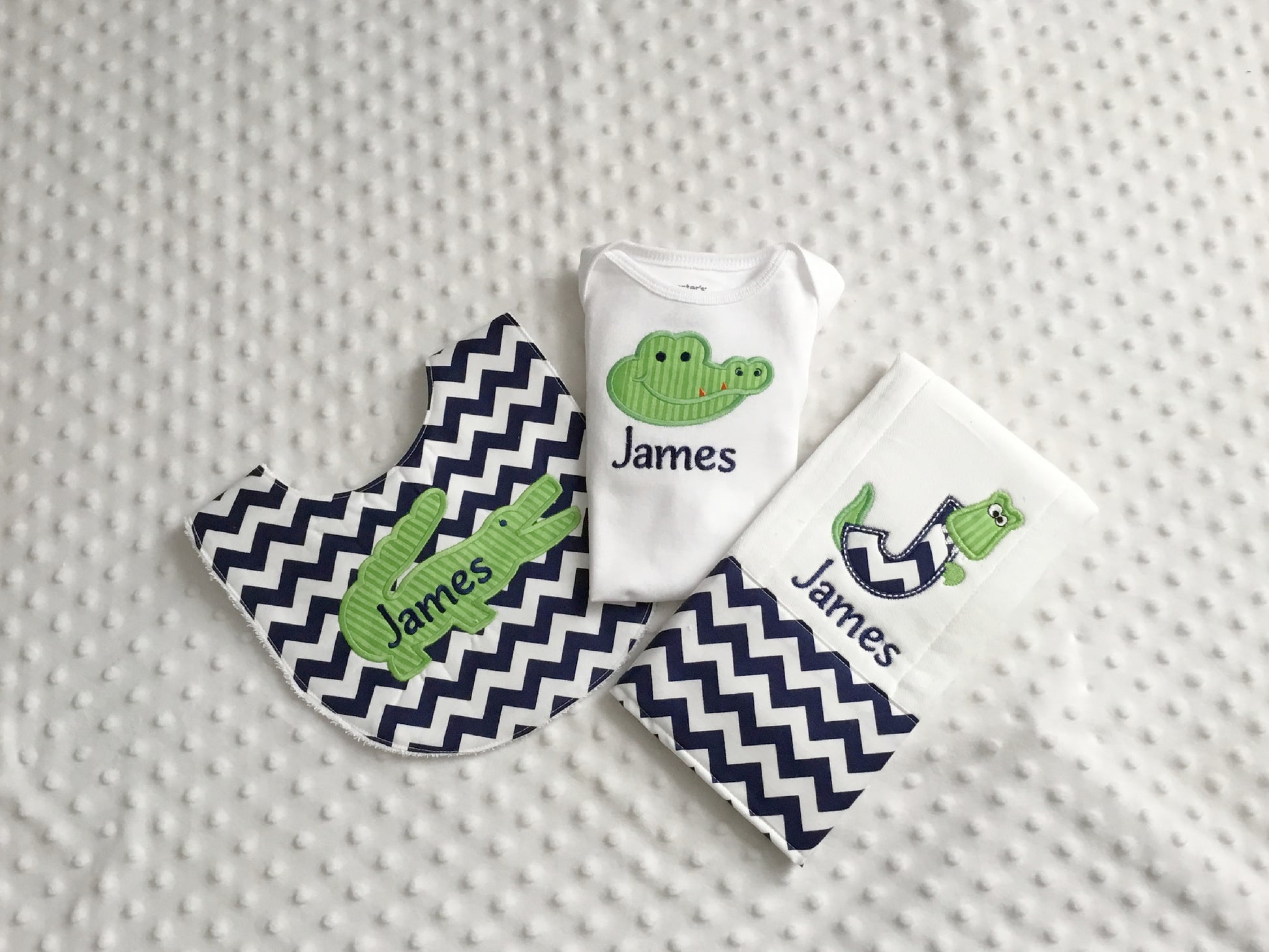 A personalized 3-piece alligator baby gift set including a white bodysuit, a navy chevron bib, and a matching monogram J burp cloth.