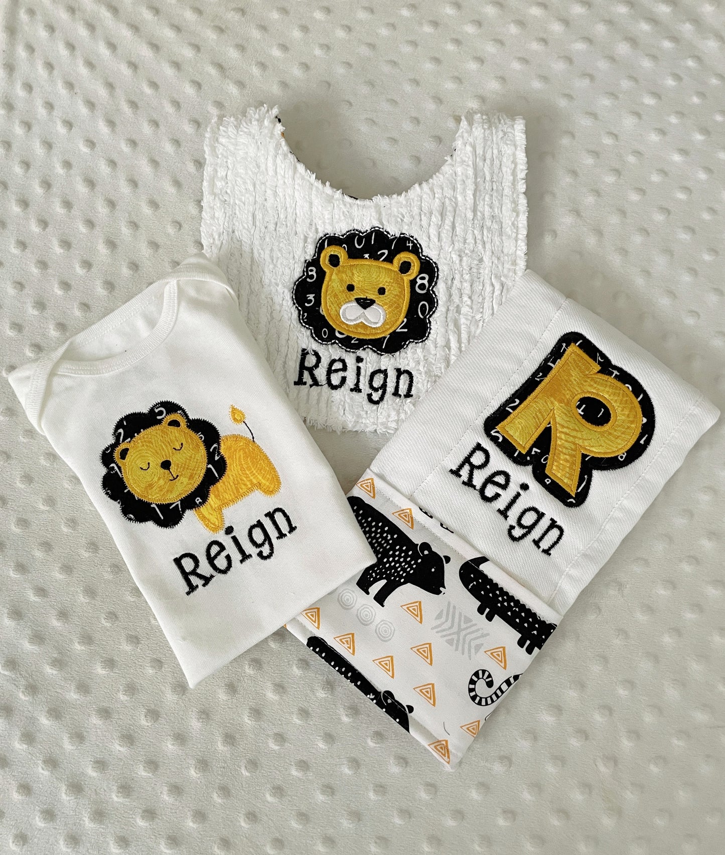 A personalized 3-piece safari lion baby gift set with a white bodysuit, a plush bib, and an initial R burp cloth for Reign.