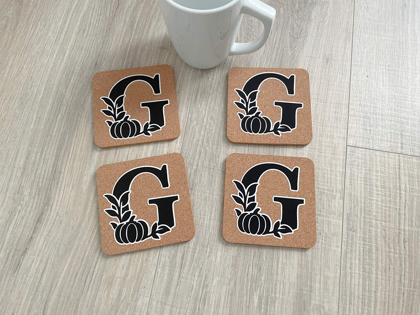 Set of four 4×4 cork coasters with monogram initial and fall pumpkin and leaf design.