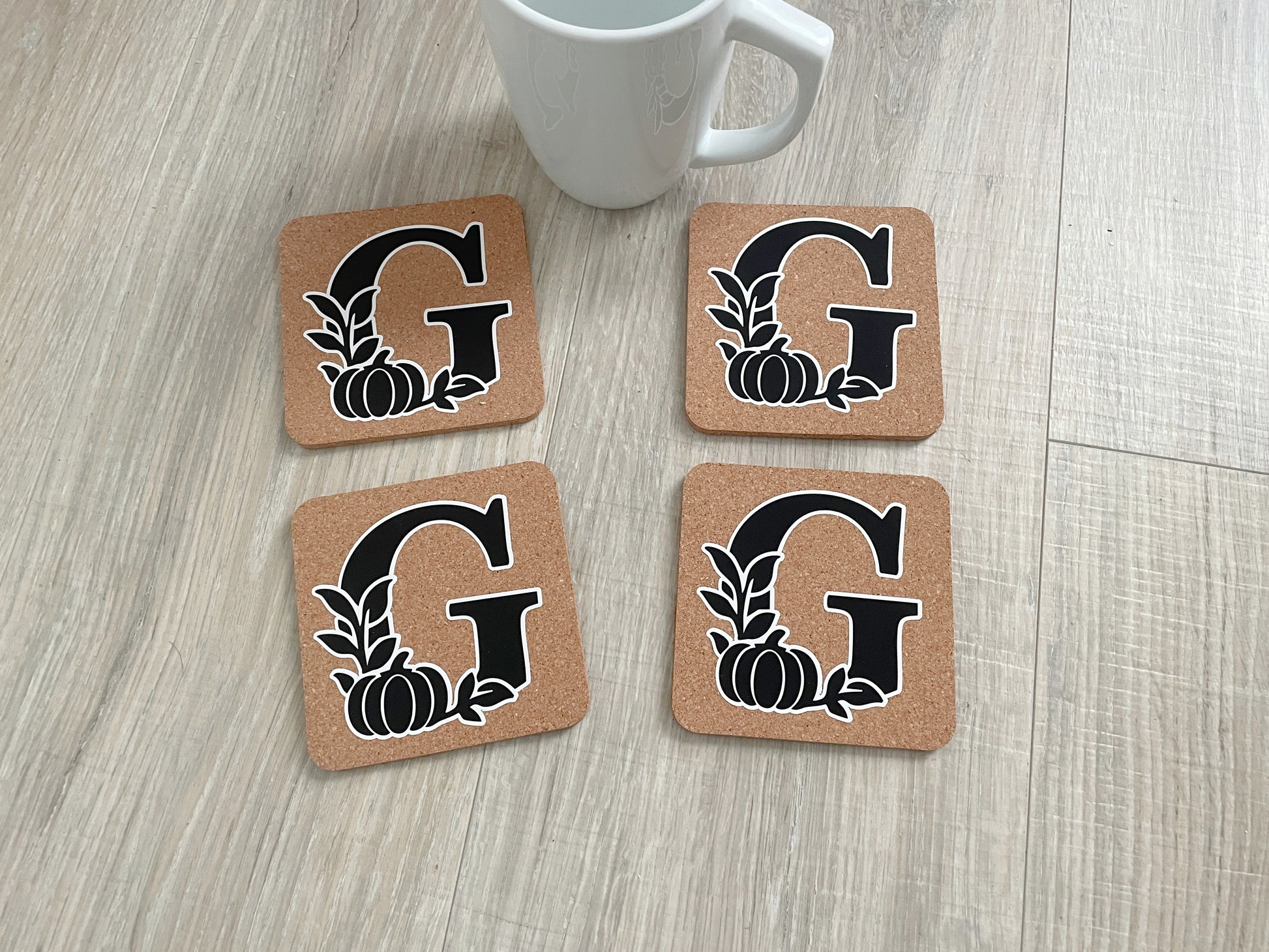 Set of four 4×4 cork coasters with monogram initial and fall pumpkin and leaf design.