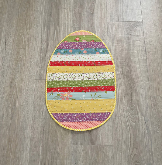 quilted table topper in the shape of an easter egg using brightly colored floral fabrics.